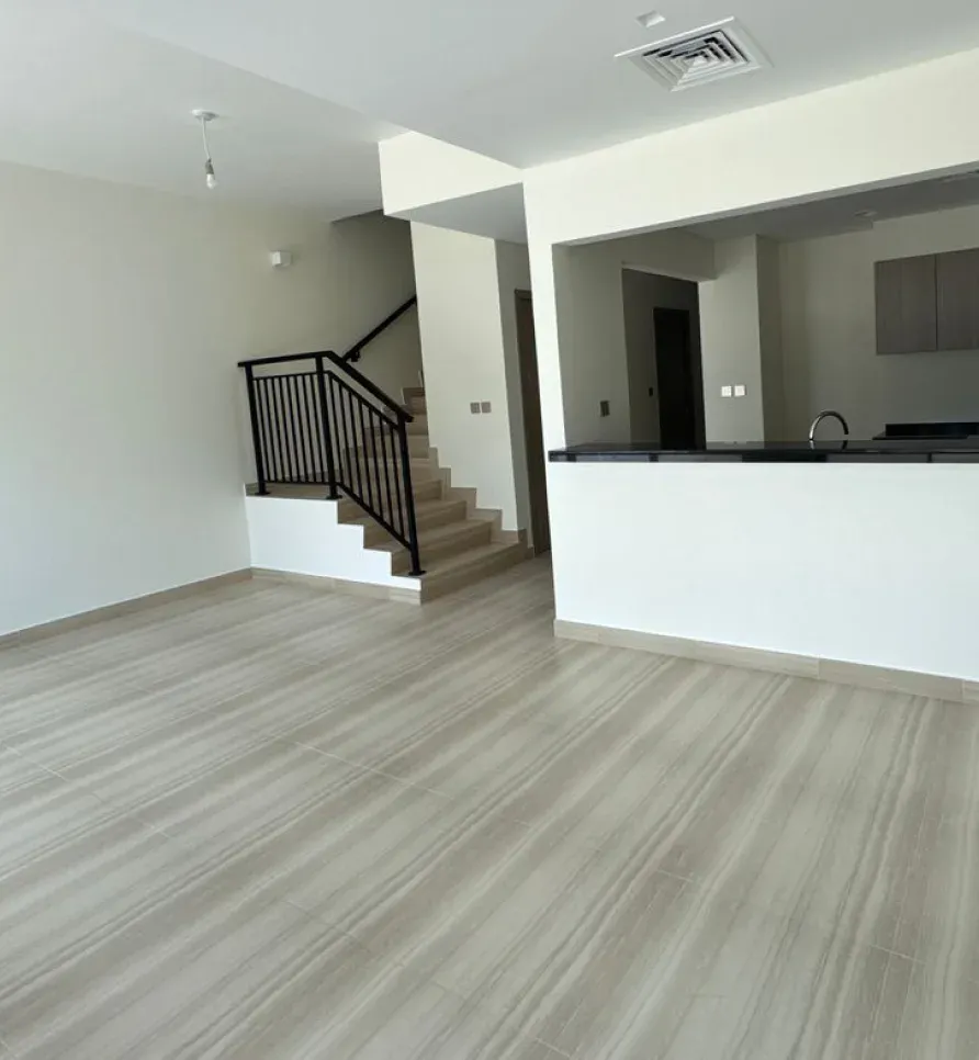 Empty open-plan living area with a staircase and a kitchen pass-through, ready for planning